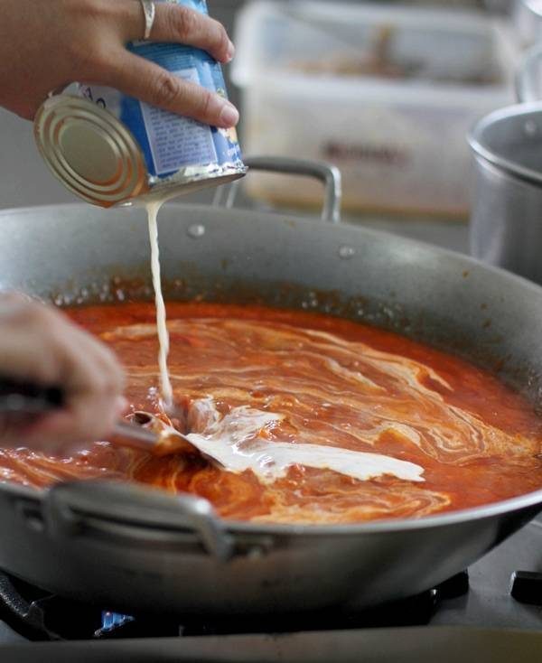 Pouring spaghetti sauce and evaporated milk to the pot.