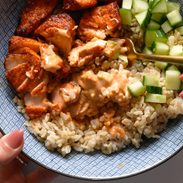 Air fryer salmon in a bowl with rice, cucumber, and sauce.