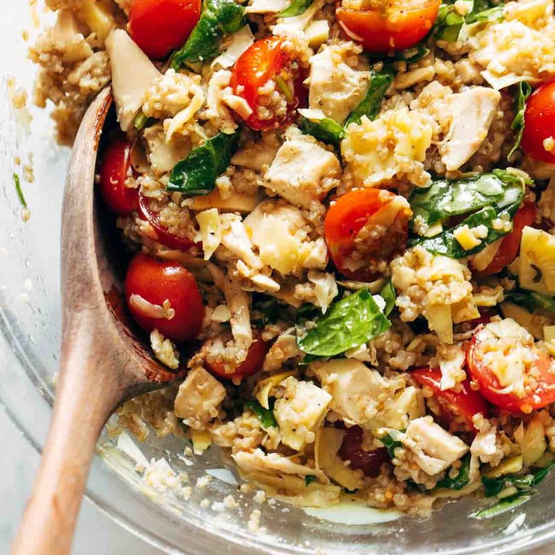 A quinoa chicken salad with tomatoes, and spinach in a glass bowl.