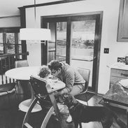 A man sitting on a chair facing a baby who is having food.