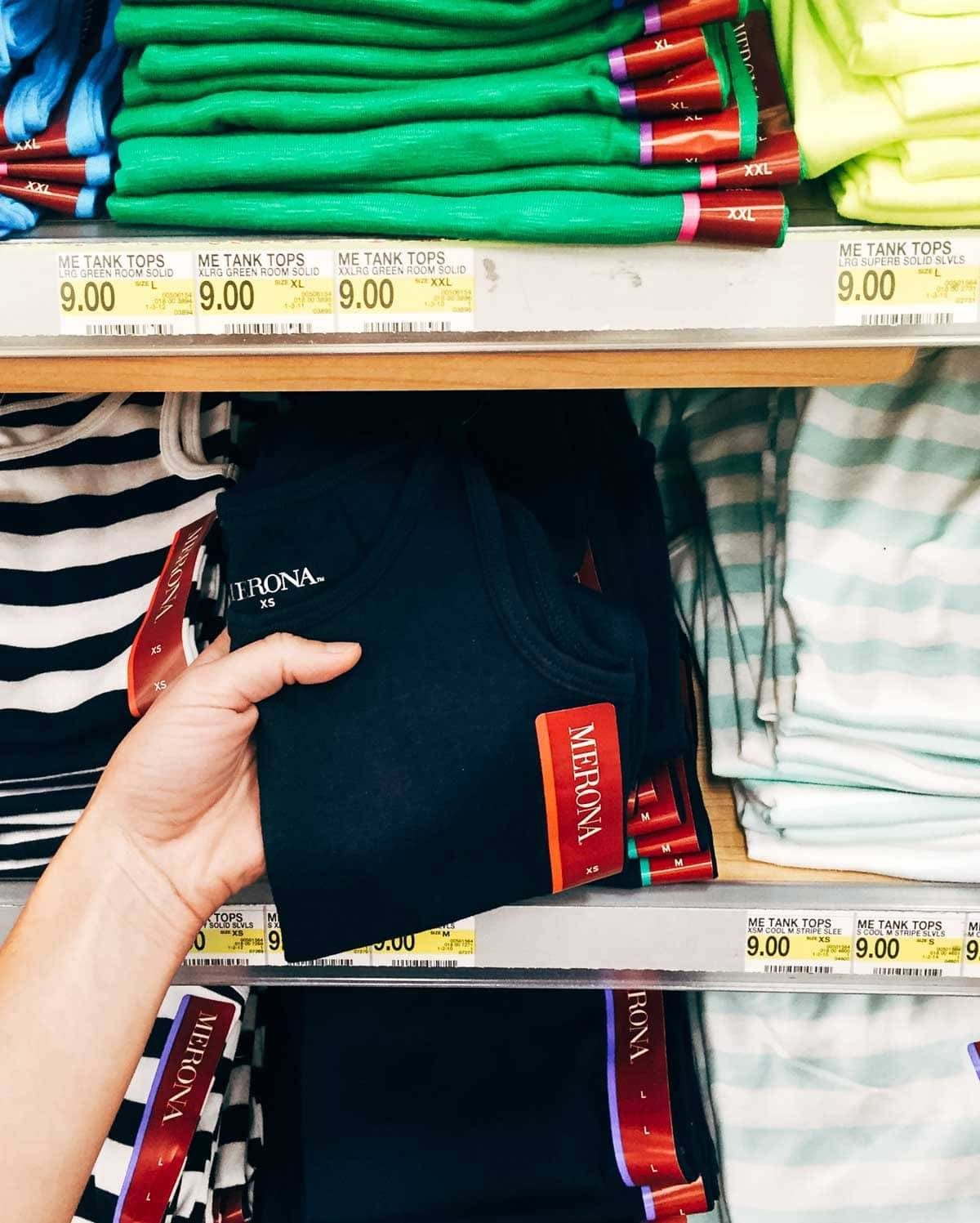 Hand holding a black tank top in a store.