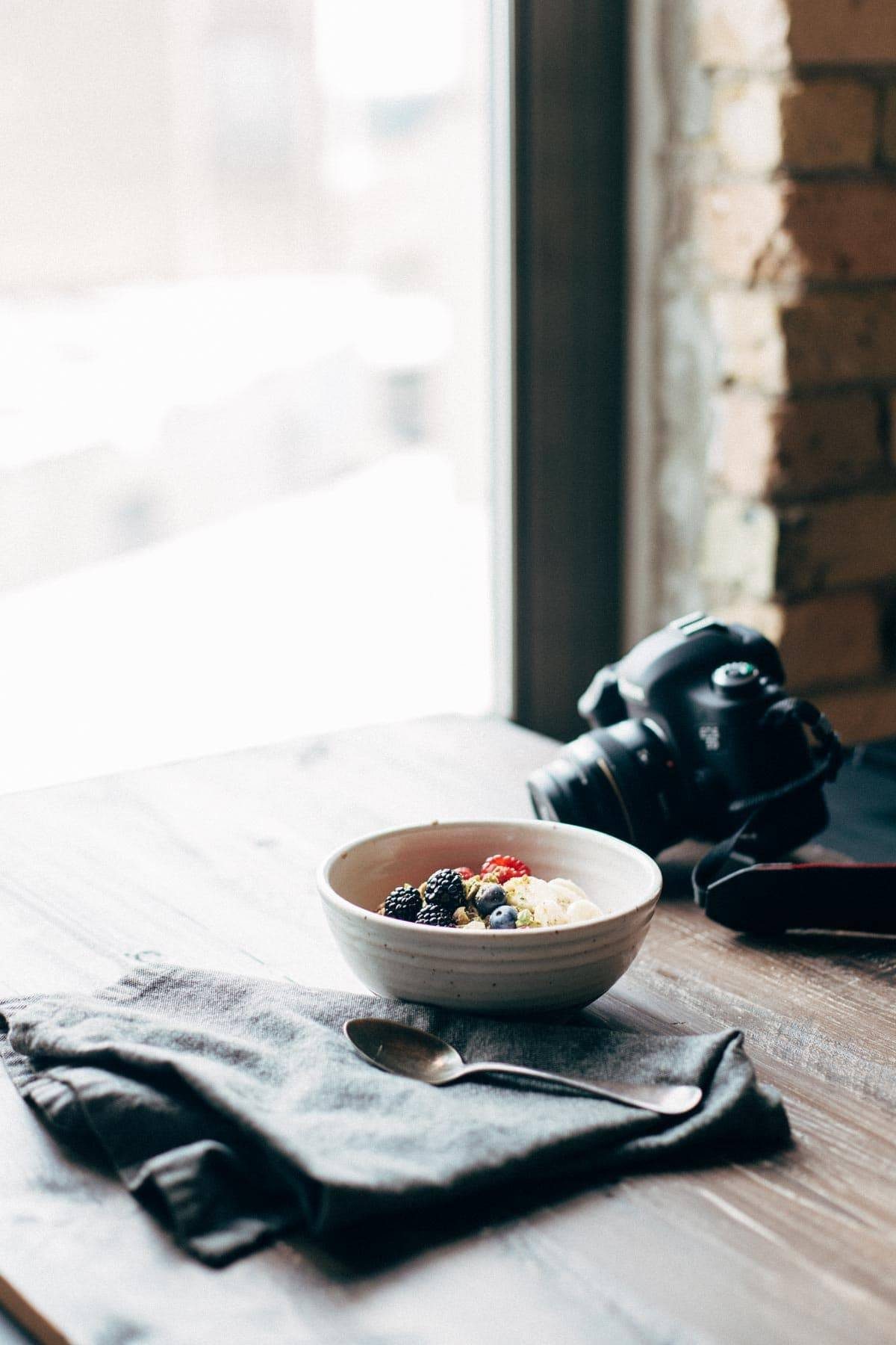 Bowl of granola and fruit on a table with a camera.