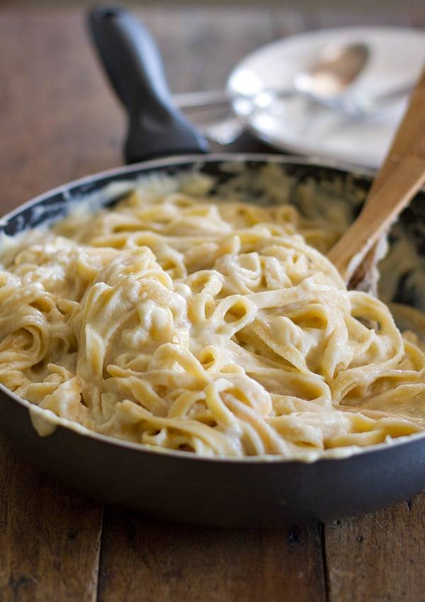 Fettuccine alfredo in a skillet with a wooden spoon.
