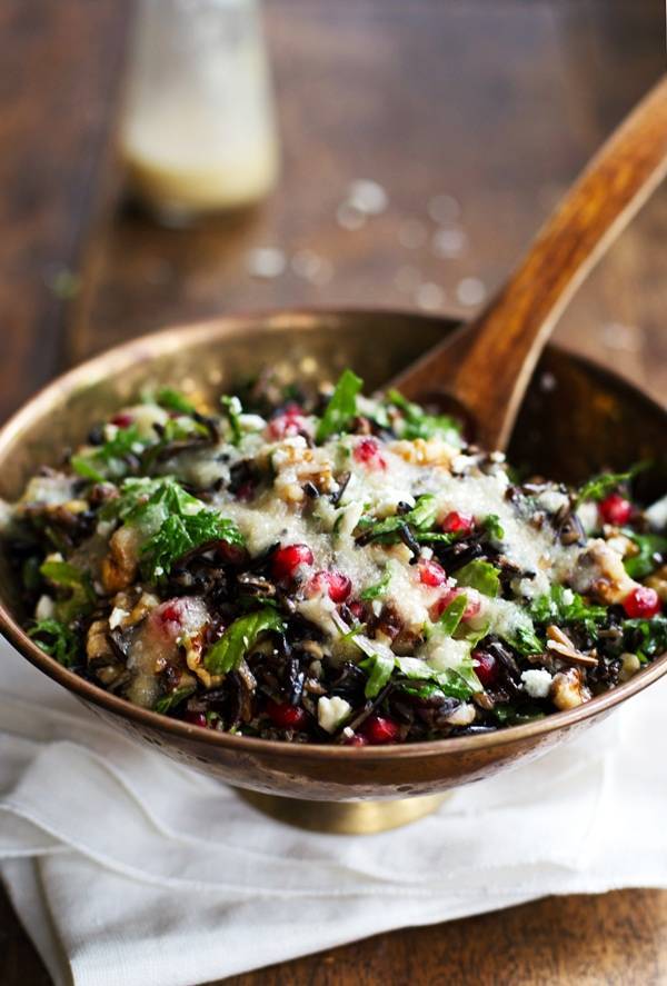 Pomegranate, Kale, and Wild Rice Salad in a bowl with a wooden spoon.