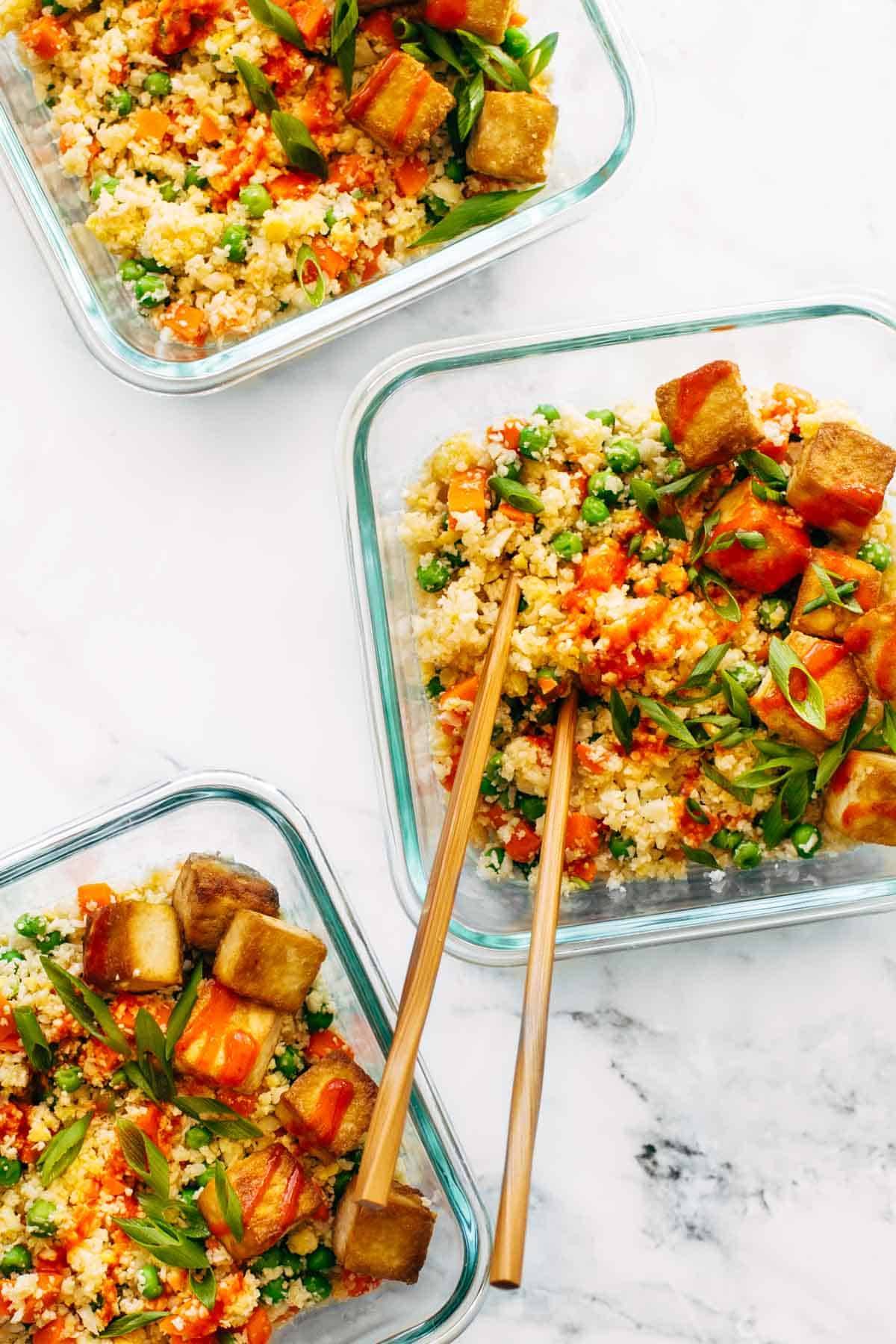 Cauliflower fried rice in meal prep containers with chopsticks.