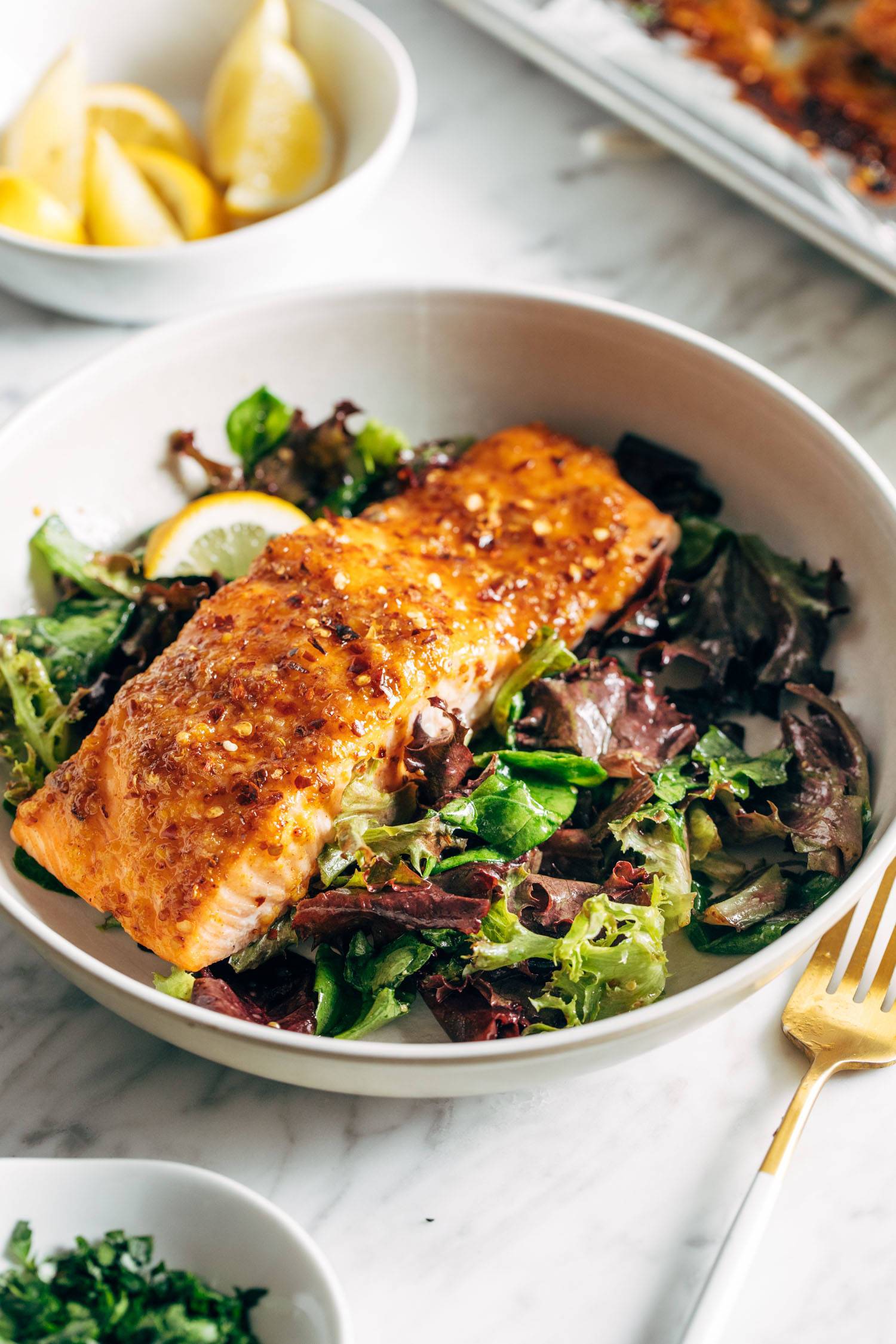 Hot honey salmon in a bowl on top of a green salad. There's a fork on the side of the bowl.
