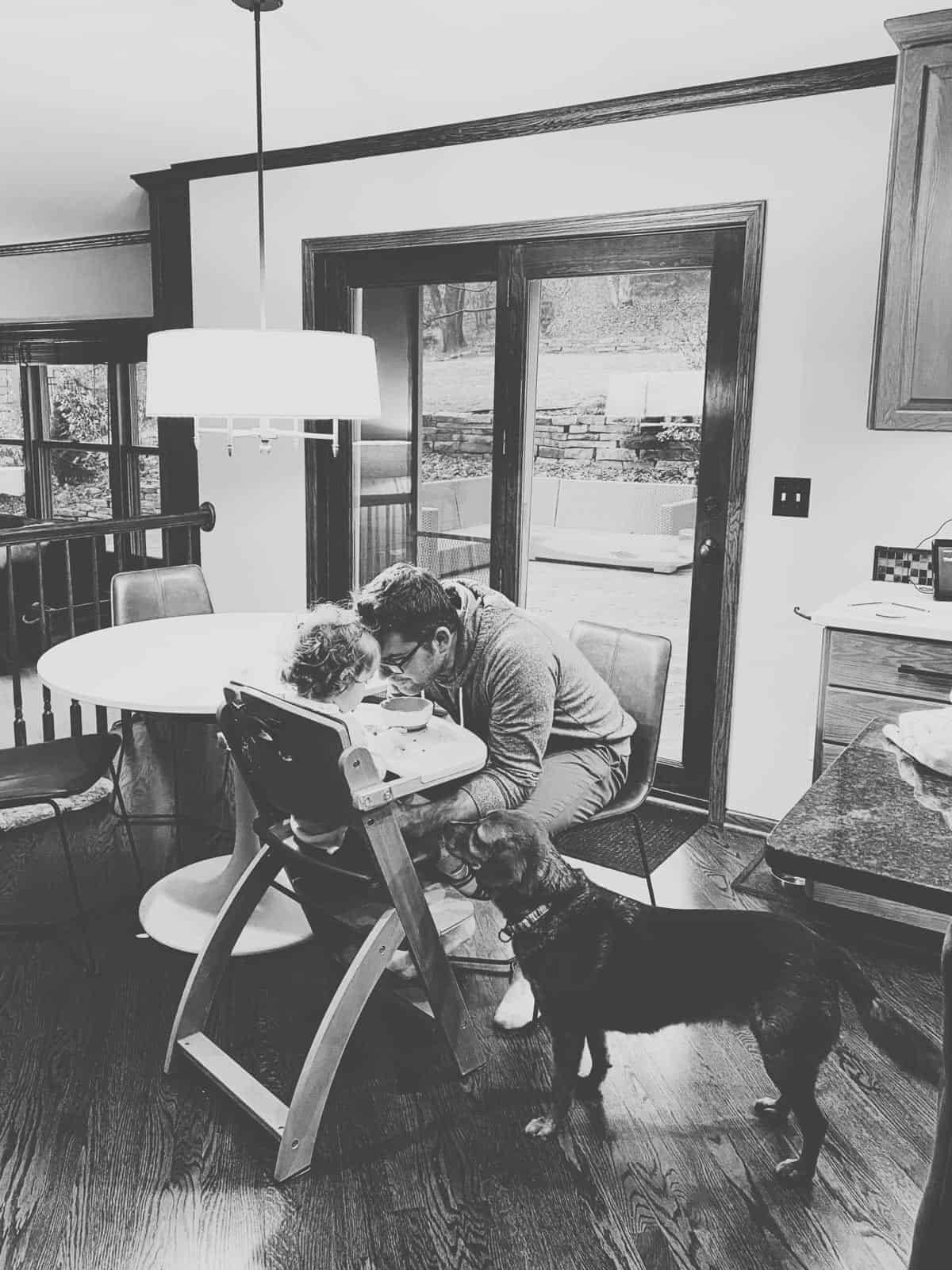 A man sitting on a chair facing a baby who is having food.