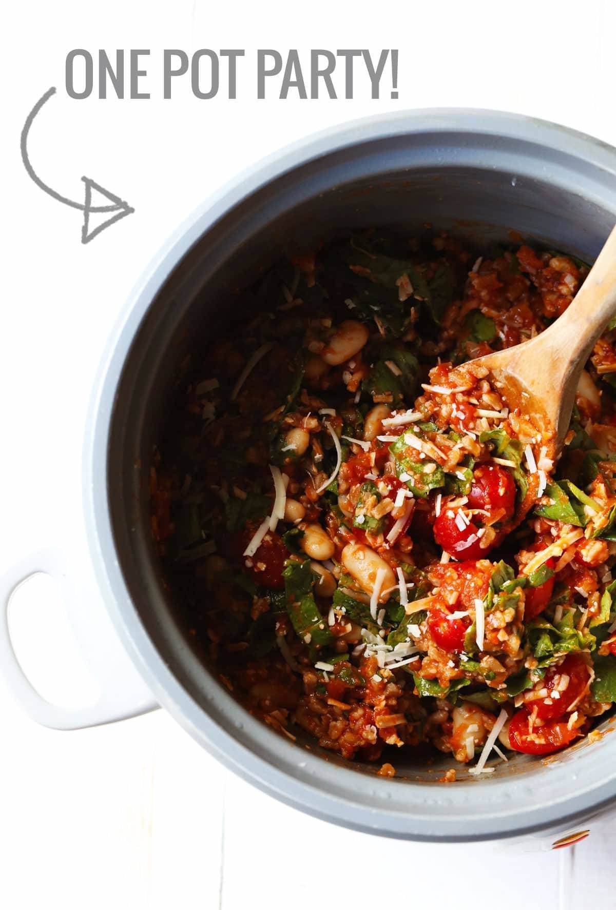 Asiago White Beans with Farro, Kale, and Tomatoes in a pot with a wooden spoon.